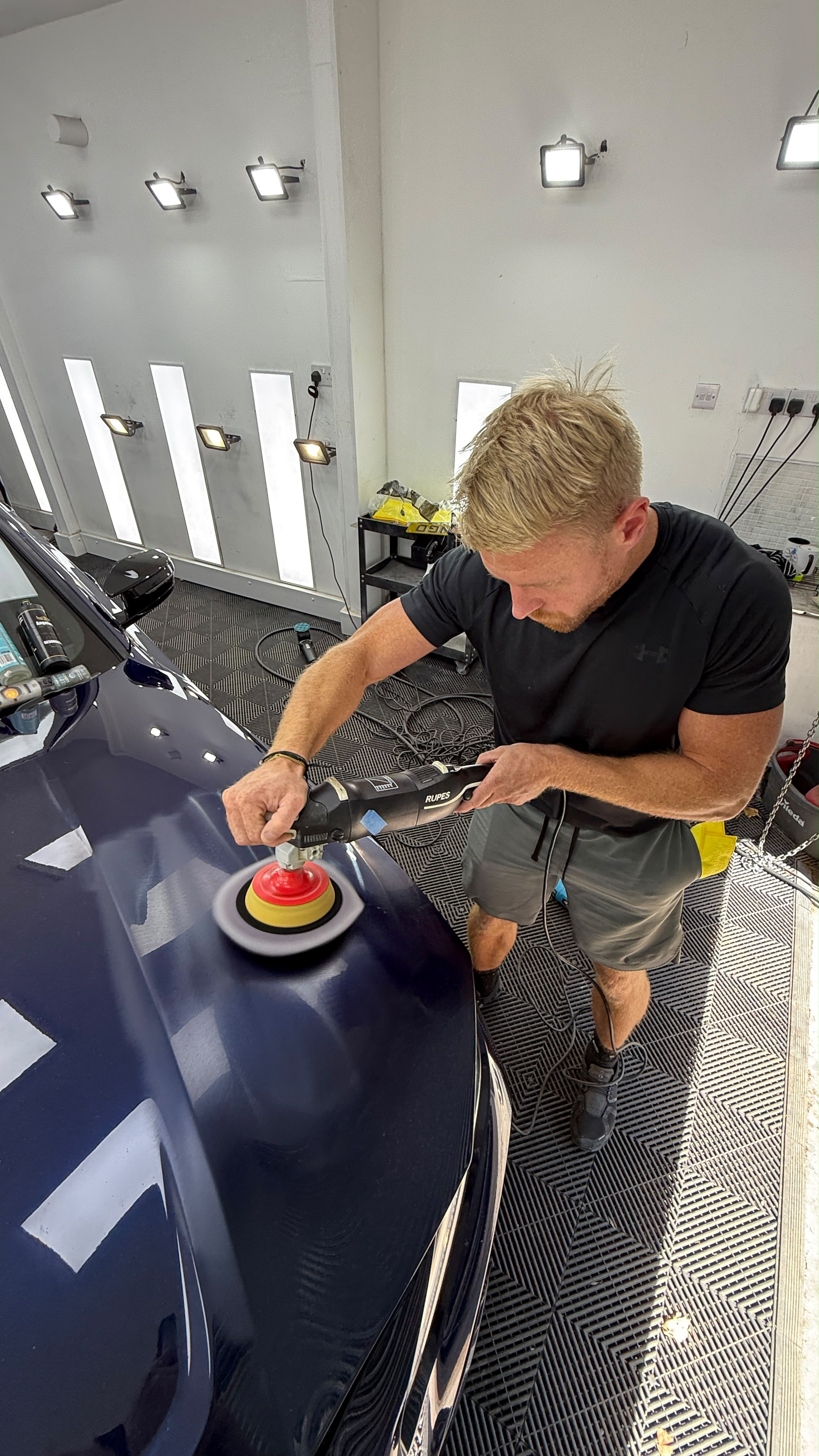 Carbon Detailing technician machine polishing a navy car in the studio